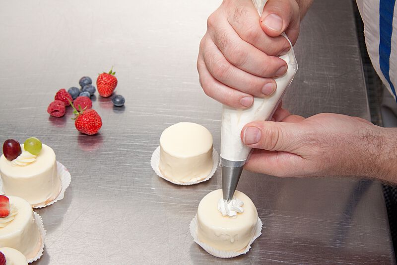 hands-applying-cream-on-small-white-round-cakes